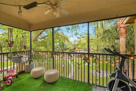 Balcony view with seating, exercise bike, and outdoor greenery.