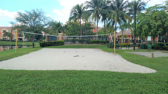 Outdoor sand volleyball court with net surrounded by grass and trees.