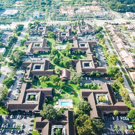 Aerial view of multiple residential buildings arranged in a grid pattern with surrounding trees and parking areas.