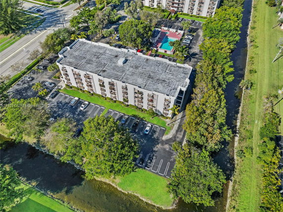 Aerial view of a multi-story apartment building with a large flat rooftop and visible parking lot.