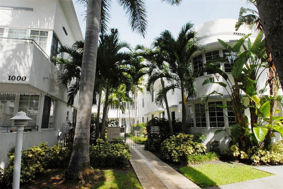 Front view of an apartment building with palm trees and a walkway.