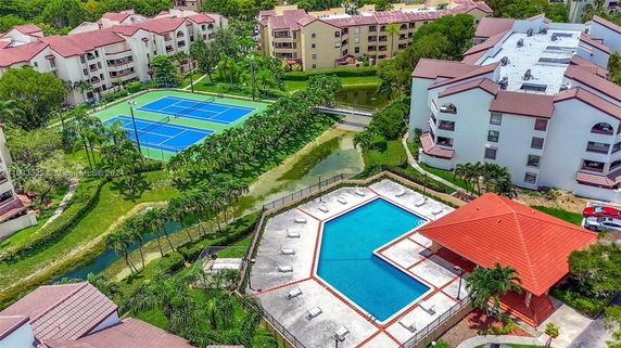 Aerial view of outdoor tennis courts adjacent to a pool area, surrounded by residential buildings.