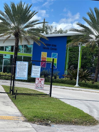 Front view of a tennis center building with colorful panels and palm trees.