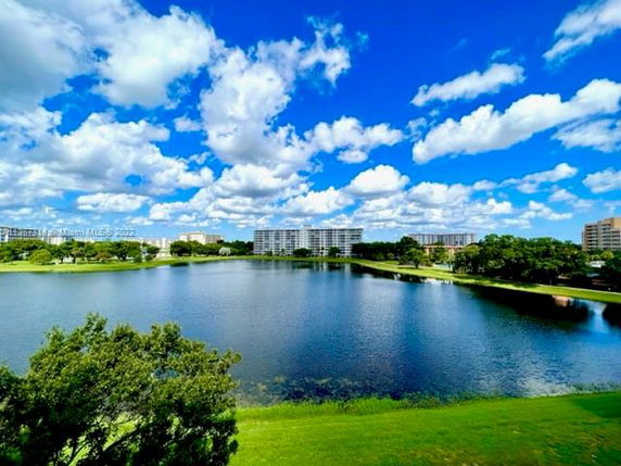 Panoramic view of a lake with buildings in the background under a blue sky with clouds.