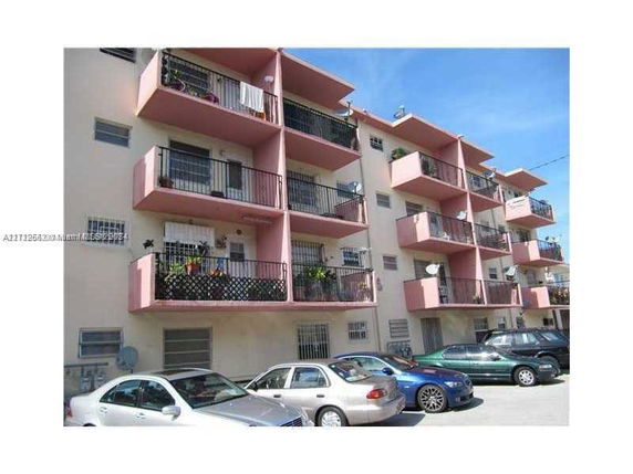 Front view of a multi-story apartment building with balconies and parked cars.