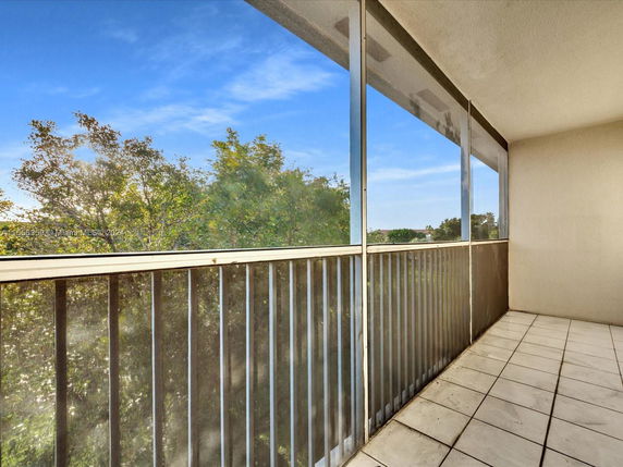 Balcony with metal railing and tiled floor, overlooking trees and clear sky.