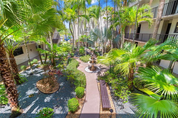Courtyard view with lush greenery and a central fountain surrounded by multi-story buildings.