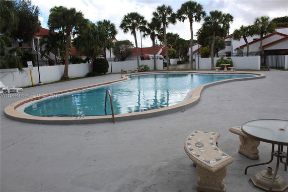 Outdoor swimming pool area with surrounding seating and palm trees.