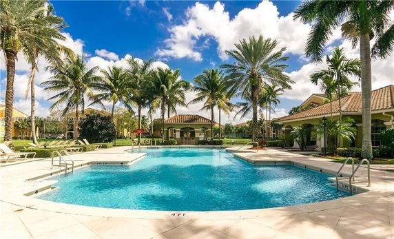 Outdoor swimming pool with palm trees and surrounding structures.