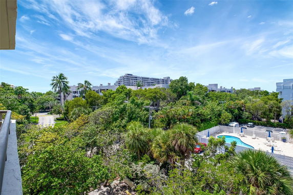 View from a building showing trees, a pool, and distant modern buildings under a blue sky.