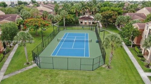 Tennis court surrounded by grass and residential buildings.