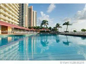 View of a high-rise building with a large pool and palm trees in the surrounding area.