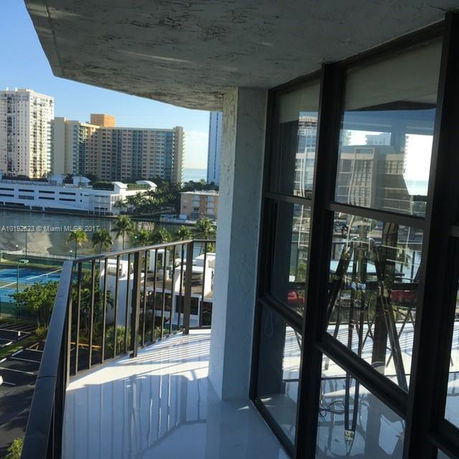 Balcony view from a high-rise building showing adjacent high-rise buildings and a glimpse of water in the distance.