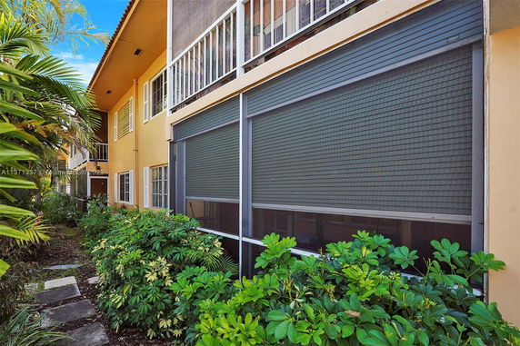 Front view of a two-story residential building with screened windows and foliage.
