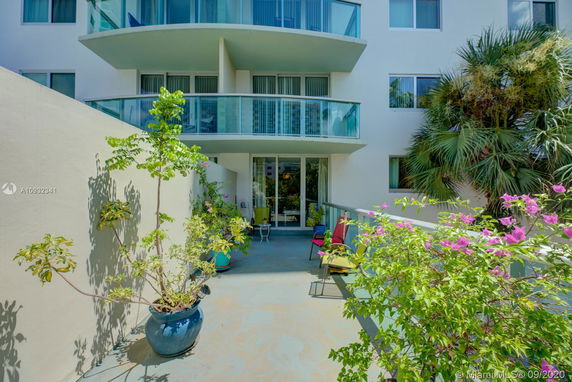 Front view of a multi-story building with curved balconies and a patio area decorated with potted plants.