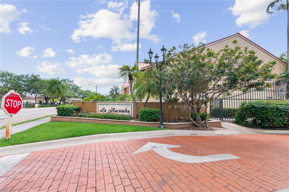 Front view of a building with a sign indicating 'La Hacienda' and a stop sign on a paved area with greenery.