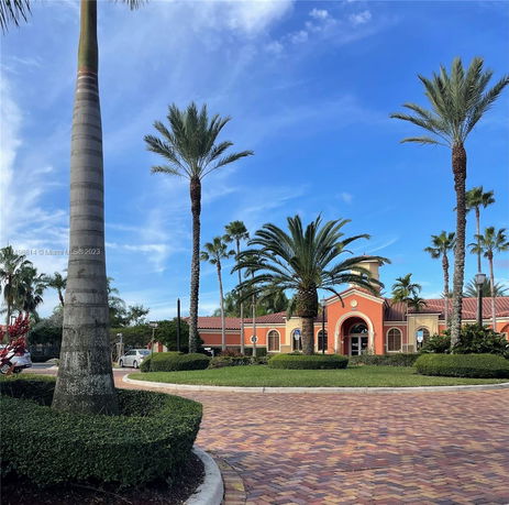 Front view of a building with a red tile roof and arched entryway, surrounded by palm trees.