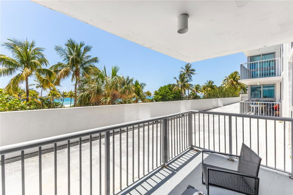 View of surrounding areas with palm trees and a distant ocean seen from a building balcony.