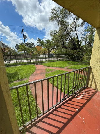View from a building showing a grassy yard and fencing with trees and buildings in the background.
