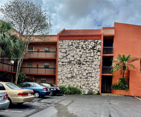 Outdoor view of a building with multiple floors and parking spaces in front.