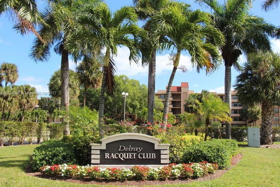 View of Delray Racquet Club sign with palm trees and buildings in the background.