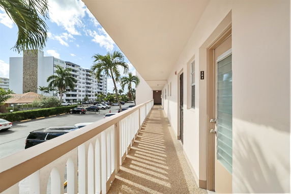 View of apartment corridor with parking area and palm trees.
