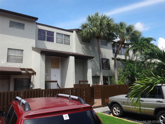 Front view of a two-story residential building with a light-colored facade and wooden fencing.