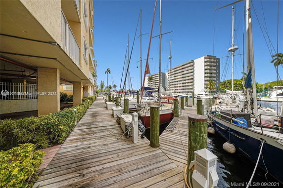 Dockside view next to buildings with multiple sailboats moored along a wooden walkway.