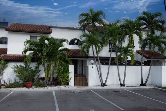 Front view of a multi-story house with a tiled roof and palm trees in front.