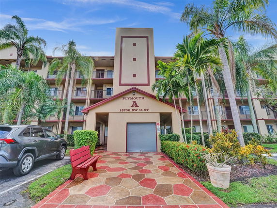 Front view of a multi-story residential building labeled Plymouth A with a parking area and landscaping.