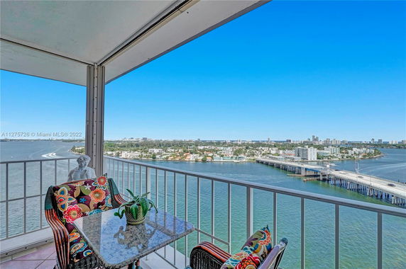 Balcony with seating overlooking a body of water and cityscape.