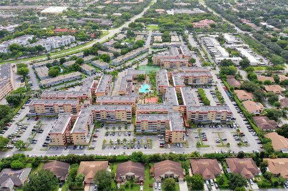 Aerial view of a large residential complex with multiple buildings and parking areas surrounded by greenery.