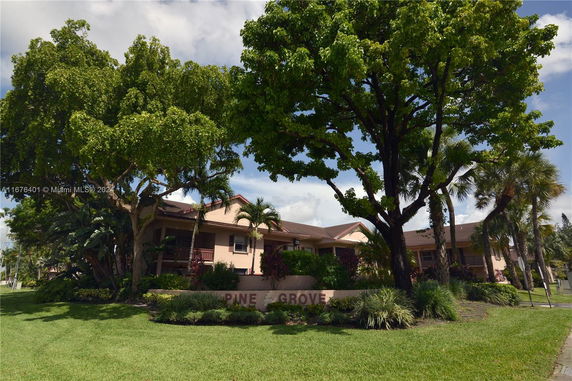 Front view of a multi-story residential building named Pine Grove with surrounding trees and plants.
