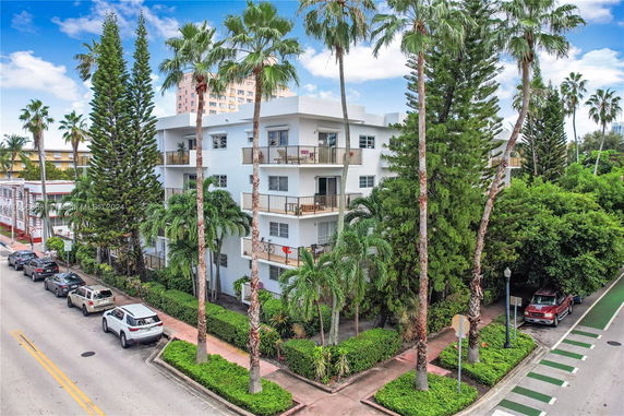 Front view of a multi-story apartment building surrounded by tall palm trees and lush greenery.
