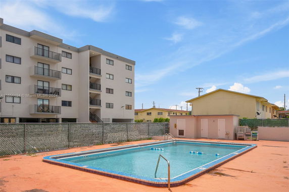 View of a rectangular outdoor swimming pool beside a multi-story residential building.