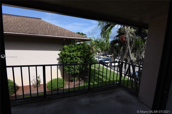 View from a balcony overlooking parking area and lush greenery.