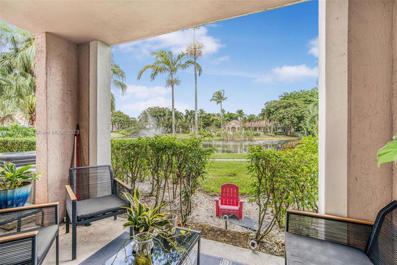 Outdoor seating area overlooking a landscaped garden with palm trees and a pond in the background.
