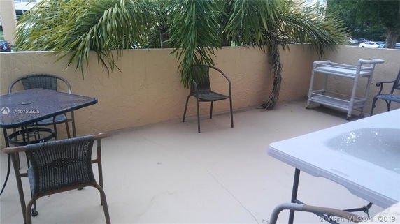 Outdoor patio area with chairs, a table, and palm tree in the background.