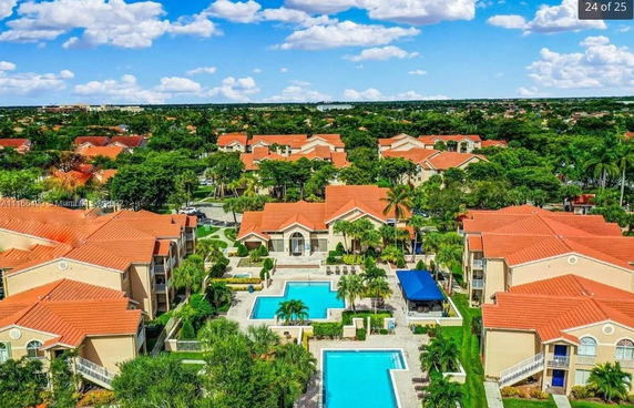 Panoramic aerial view of a residential complex with swimming pools and red-roofed buildings.