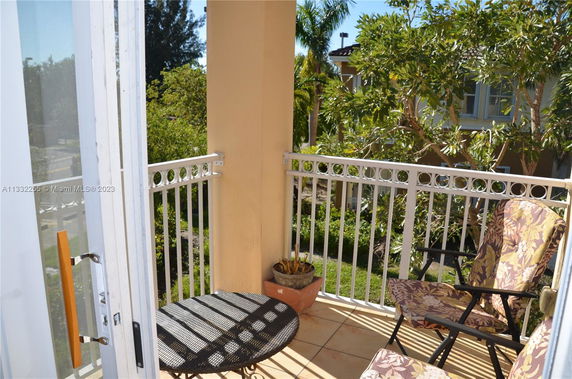 Balcony with outdoor chairs and table, view of trees and building.
