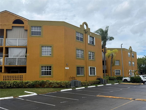 Front view of a three-story apartment building with a mustard and green color scheme.