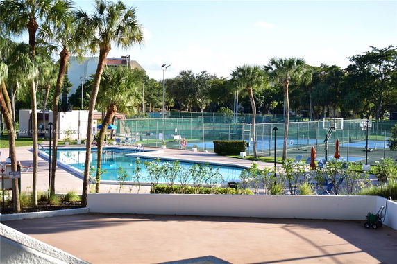 Outdoor area with swimming pool and tennis courts surrounded by palm trees.