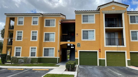 Front view of a three-story apartment building with balconies and two garages on the ground floor.