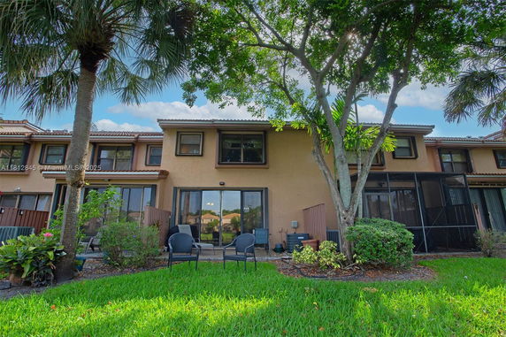 Rear view of a two-story townhouse with a patio and lawn area.