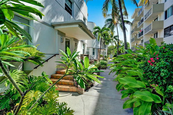 Front view of a multi-story building with steps leading to the entrance, surrounded by tropical plants.
