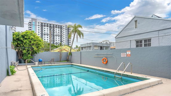 Outdoor swimming pool with surrounding patio and buildings in the background.