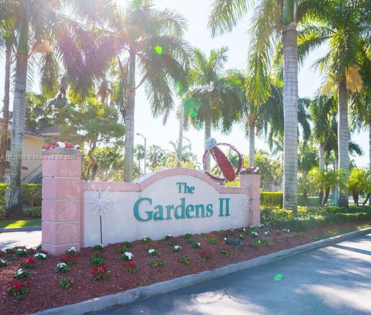 Entrance sign for The Gardens II surrounded by palm trees.
