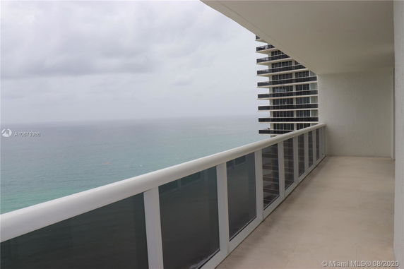 Panoramic view from a balcony overlooking the ocean with a partial view of a neighboring building.