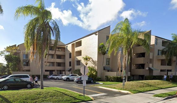 Front view of a multi-story residential building with balconies and surrounding palm trees.