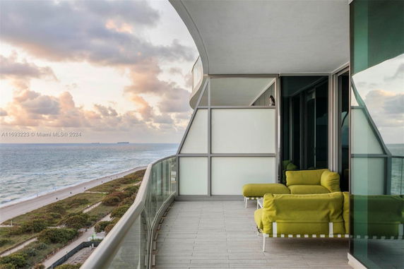 Panoramic view from a high-rise balcony overlooking the ocean with a seating area.